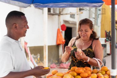 Canlı bir meyve standında alışveriş yaparken taze mandalinadan zevk alan bir kadın.