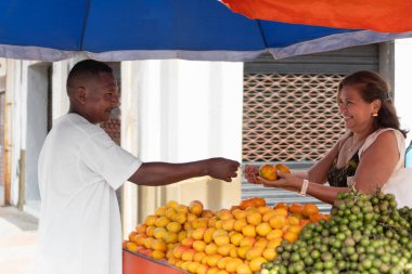 Tedarikçi canlı bir cadde pazarında gülümseyen bir müşteriye taze portakal satıyor.