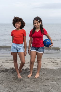 Yaz tatilinin tadını çıkaran kızlar ellerinde futbol topu tutuyorlar.