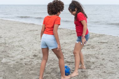 Genç kızlar deniz kenarındaki kumsalda top oynarken eğleniyorlar.