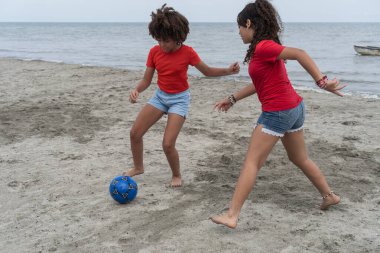 Sahilde çıplak ayakla futbol oynayan iki kız çocukluk ve arkadaşlığın tadını çıkarıyor.