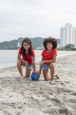 Kumsalda futbol topuyla oynayan iki mutlu kız.