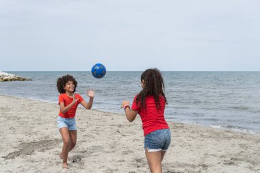 Deniz kenarındaki kumsalda mavi topla oynayan iki kız.
