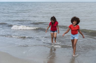 Gülümseyen çeşitli kızlar yaz tatilinde okyanus dalgalarında oynuyorlar.
