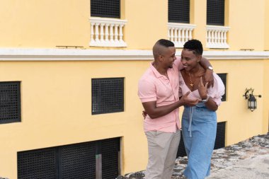 Sarı bir binanın önünde gülüşen mutlu siyah çift yolculuklarının keyfini çıkarıyorlar.