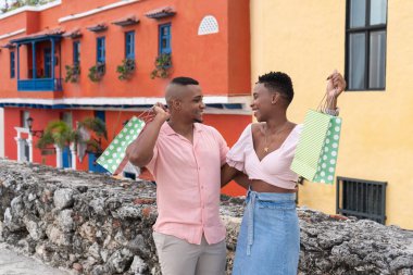 Mutlu siyah çift renkli bir caddede alışveriş torbaları taşıyor.