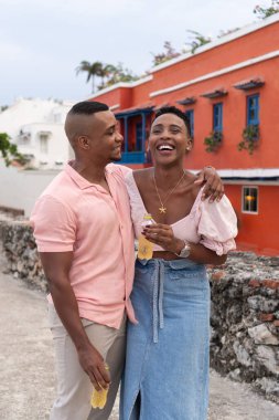 Siyahi çift kucaklaşıp gülüyor, tatilde içkilerini paylaşıyor.