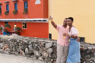 Mutlu siyah çift, tropikal tatillerinde içki içerken selfie için poz veriyor.