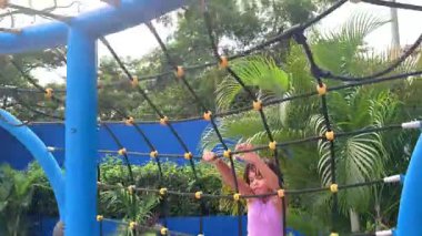 Mutlu küçük kız dışarıda bir oyun bahçesinde ipe tırmanırken eğleniyor.