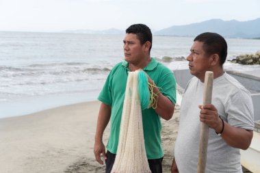 İki İspanyol balıkçı kumlu bir sahilde elinde balık ağıyla okyanusa bakıyor.