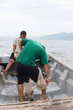 Teknede çalışan balıkçılar, balık dolu bir oltayı elle çekiyorlar.