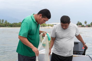 İki balıkçı birlikte çalışıyor, küçük teknelerinde bir balık ağını çözüyorlar.