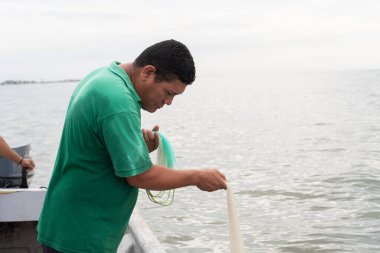 Bir teknede çalışan balıkçı, suya balık ağı atıyor.