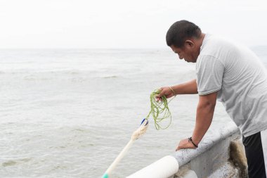 Adam beton bir iskeleden denize atmadan önce balık ağını hazırlıyor.