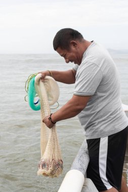 Balıkçı gülümsüyor, denizden balıklarla dolu bir ağ çekiyor.