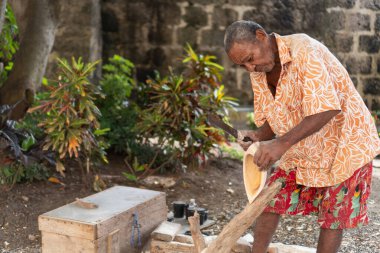 Yaşlı bir zanaatkar ustalıkla ahşap bir kase oyuyor, geleneksel sanatını icra ediyor.