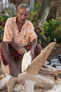 Ahşap heykeli şekillendiren yaşlı bir adam, geleneksel zanaatı gösteriyor.