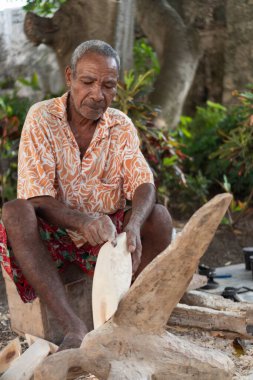 Ahşap heykeli şekillendiren yaşlı bir adam, geleneksel zanaat ve odaklanmış beceri gösteriyor.