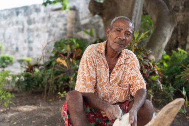 Yaşlı esnaf odun yontuyor, geleneksel kültür ve el becerisini temsil ediyor.