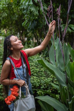Yeşil bir bahçede turuncu güller taşıyan sakin ve mutlu bir kadın doğayı keşfediyor.