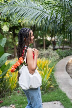 Çantasında gül taşıyan bir kadın, tropikal bir parkta dikkatli bir rutini kucaklıyor.