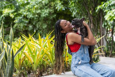 Tulumlu kadın köpeğini kucaklıyor, doğada neşe ve arkadaşlık buluyor.