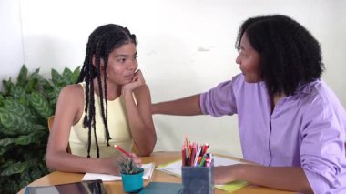 Afrikalı Amerikalı anne, evde ödevlerine yardım ederken sıkılmış genç kızını teselli ediyor.