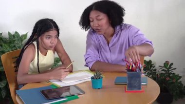 Önemseyen siyah anne, küçük kızına okul dersleri ve ödev için ahşap bir masada yardım ediyor.