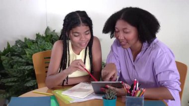 Genç kız ve annesi bir masada e-öğrenim için dijital tablet kullanarak birlikte okuyorlar.