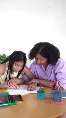 Genç kızına ödevlerinde yardım eden, tahta bir masada kağıt üzerine çizen siyahi bir kadın.