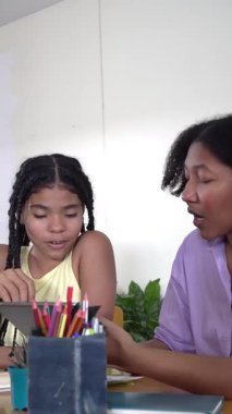 Bakıcı anne, genç kızına dijital tabletle evde e-öğrenme konusunda yardım ediyor.