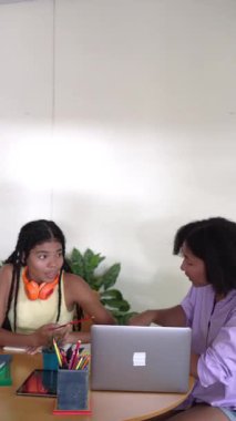 İki farklı genç kız birlikte okuyorlar, bir dizüstü bilgisayar kullanıyorlar ve ödevlerini tartışıyorlar.