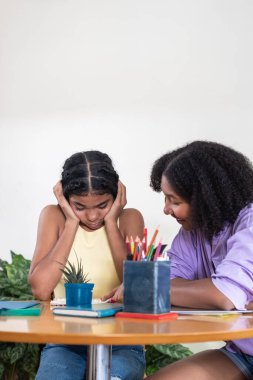 İki kız birlikte çalışıyor, biri açıklarken diğeri üzgün ya da şaşkın görünüyor.