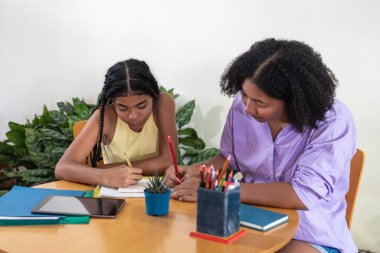 Yetişkin bir kadın okul ödevlerinde genç bir kıza masa başında yardım ediyor.