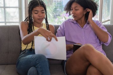 Kanepede oturan genç öğrenciler, kağıt üzerinde çizelgeyi tartışıyorlar, eğitime ve yeni çalışmalara odaklanıyorlar.