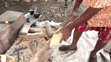 Yetenekli bir zanaatkar açık hava atölyesinde geleneksel bir el aletiyle bir tahta parçasını dikkatlice şekillendiriyor.