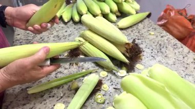 Çiftçinin elleri kabuk bağlıyor ve mutfak tezgahında taze mısır kesiyor.