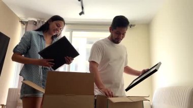 Genç mutlu çift yeni dairelerine taşınırken karton kutulardan resim çerçevelerini açıyor.