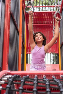 Renkli bir oyun bahçesinde, maymun parmaklıklarında gülümseyen genç bir kız.