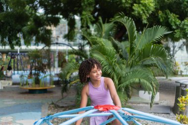 Parktaki tırmanma parkında gülümseyen genç kız, yaz oyununun tadını çıkarıyor.