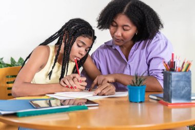 Yetişkin bir kadın, genç bir kıza özel ders veriyor. Eğitim sırasında defterine işaret ediyor.