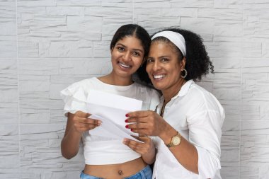 Genç bir kadın ve anne muzaffer bir şekilde ellerinde bir üniversite kabul mektubu tutuyorlar, bir başarı anını paylaşıyorlar.