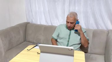 Oturma odasındaki kanepede uzaktan çalışan, tablet ve cep telefonuyla birden fazla iş yapan kıdemli bir adam.