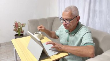 Üst düzey bir adam oturma odasındaki kanepede oturup bir fincan kahve içerken tableti karıştırıyor.