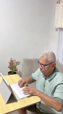 Yaşlı adam oturma odasındaki tablet bilgisayar klavyesinde yazarken konsantre oluyor.
