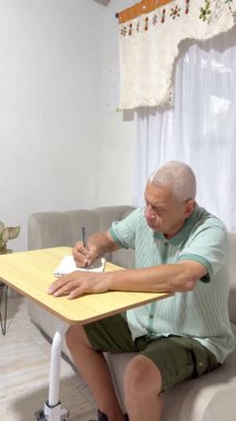 Kanepede oturan kıdemli bir adam, günlük rutinini ve düşüncelerini evdeki bir deftere yazıyor.