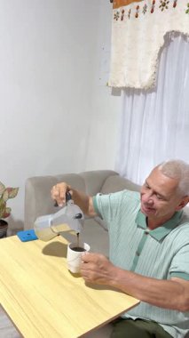 Gülümseyen kıdemli adam günlük sabah rutininin tadını çıkarıyor. Evdeki bir çaydanlıktan kahve doldurup içiyor.