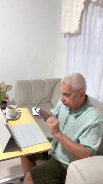 Tablet üzerinde çalışıp evde kahve içmeden önce gözlüğünü temizleyen yaşlı bir serbest yazar.