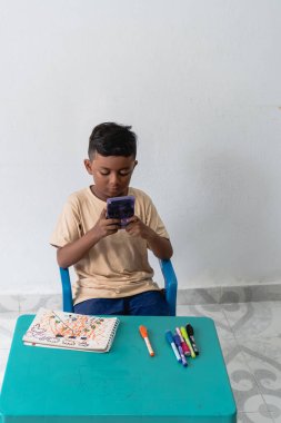 Küçük bir masada geleneksel öğrenme faaliyetleri yerine dijital eğlenceyi seçen bir çocuk