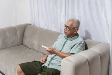 Uzaktan kumandalı yaşlı bir adam, bir kanepede oturuyor, boş zamanların tadını çıkarıyor.